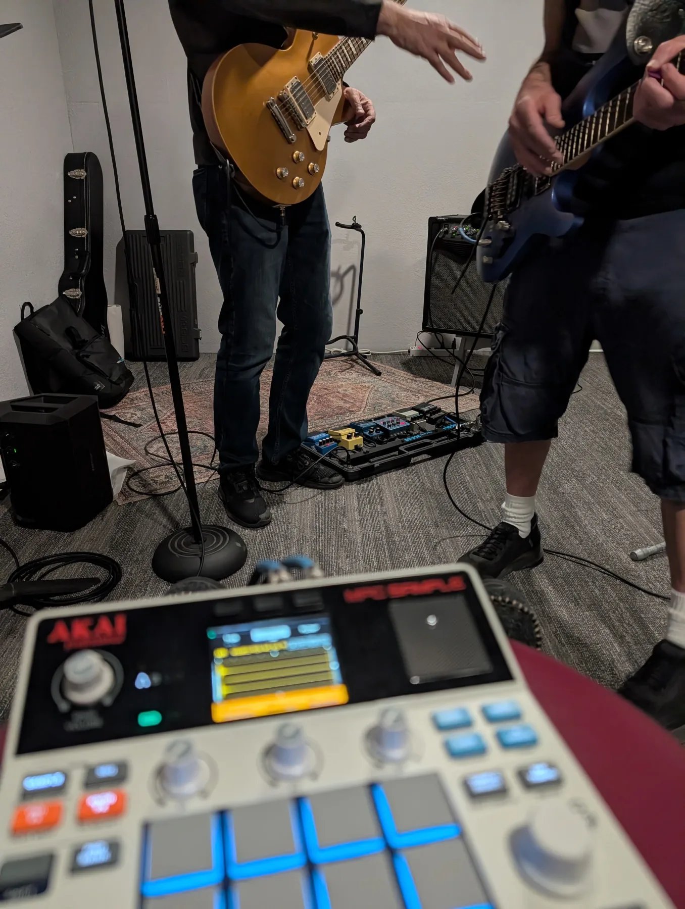An Akai MPC pad controller in the foreground during a band rehearsal with two guitarists