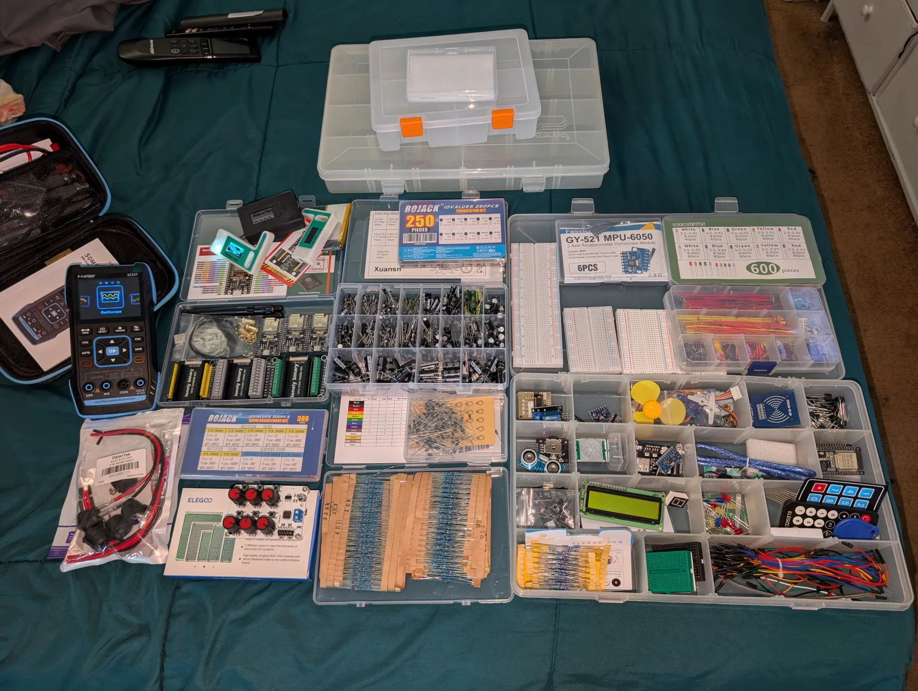 Electronics components, breadboards, test equipment, and parts organized across a bed