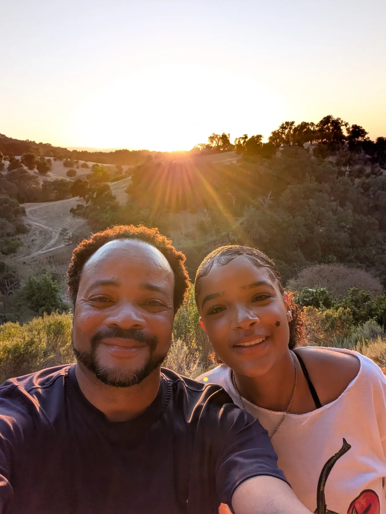 Warren Blackwell and his daughter smiling together in front of a hillside sunset