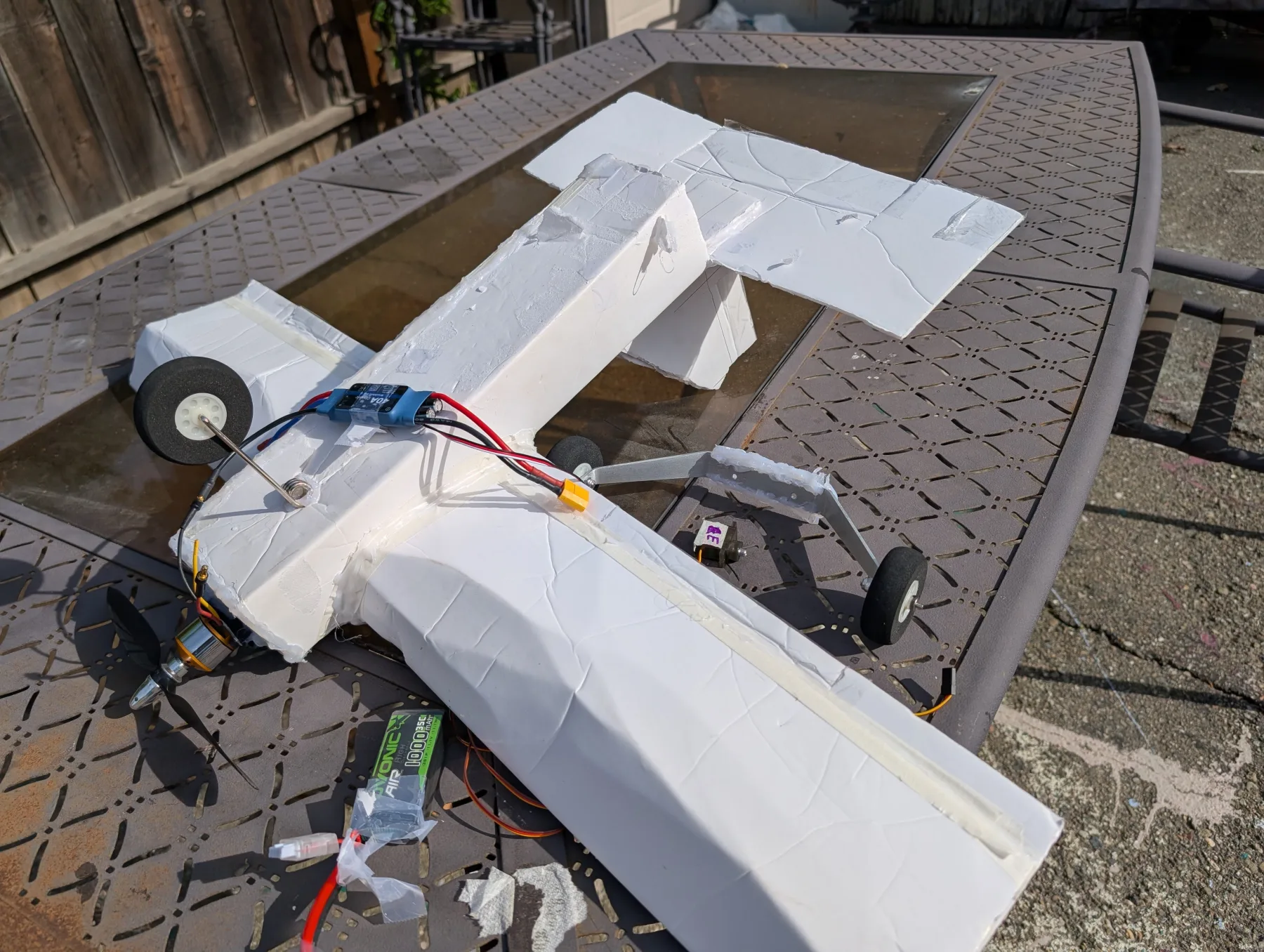 A damaged handmade foamboard RC airplane resting on a backyard table