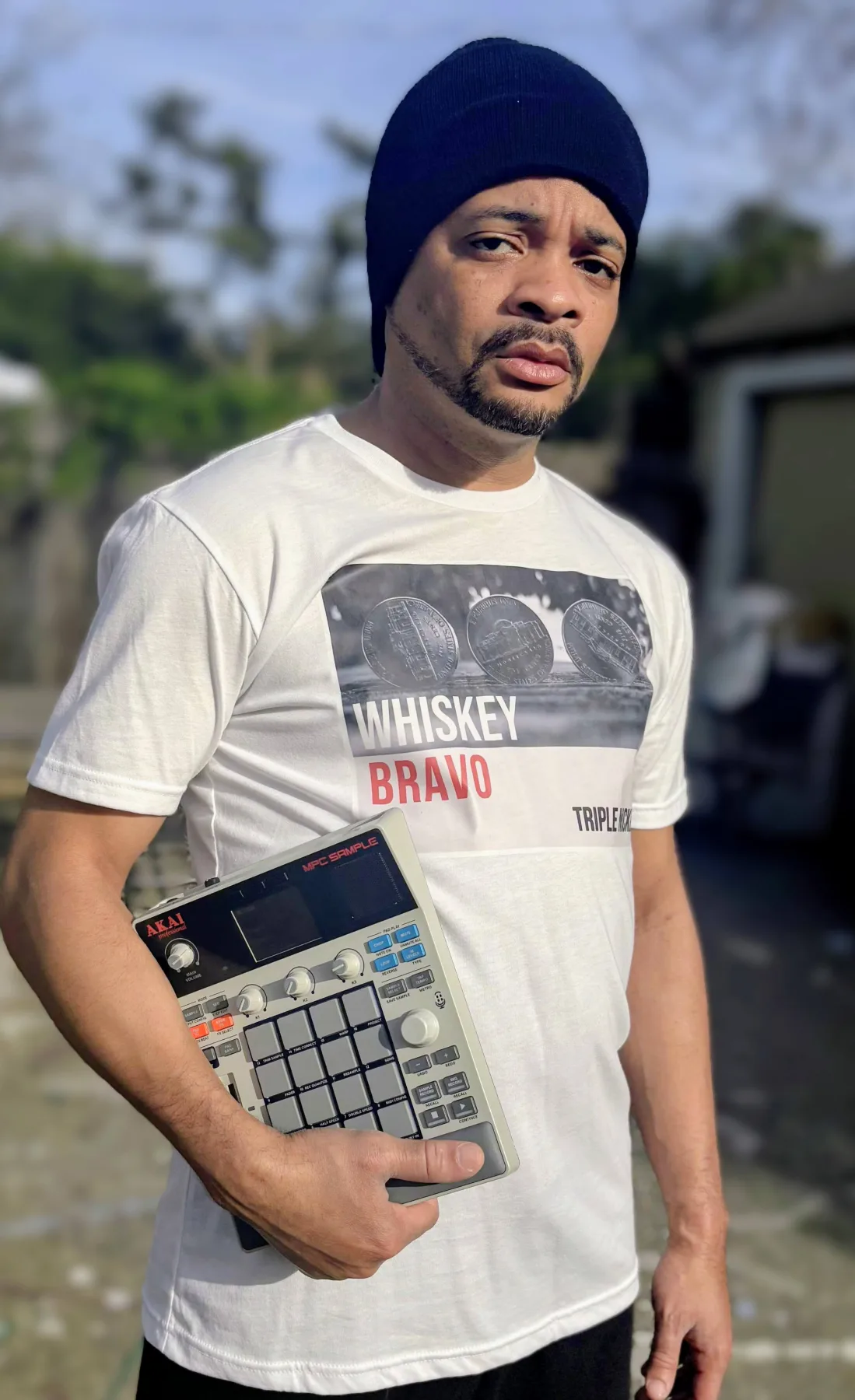 Warren standing outside holding a compact Akai MPC music sampler