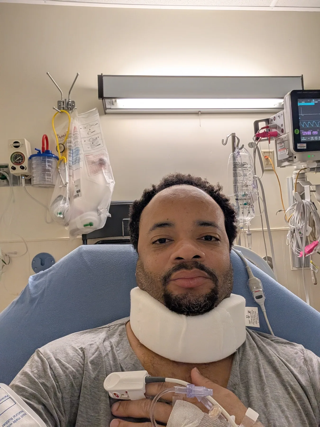 Warren awake in a hospital recovery room wearing a neck brace after surgery