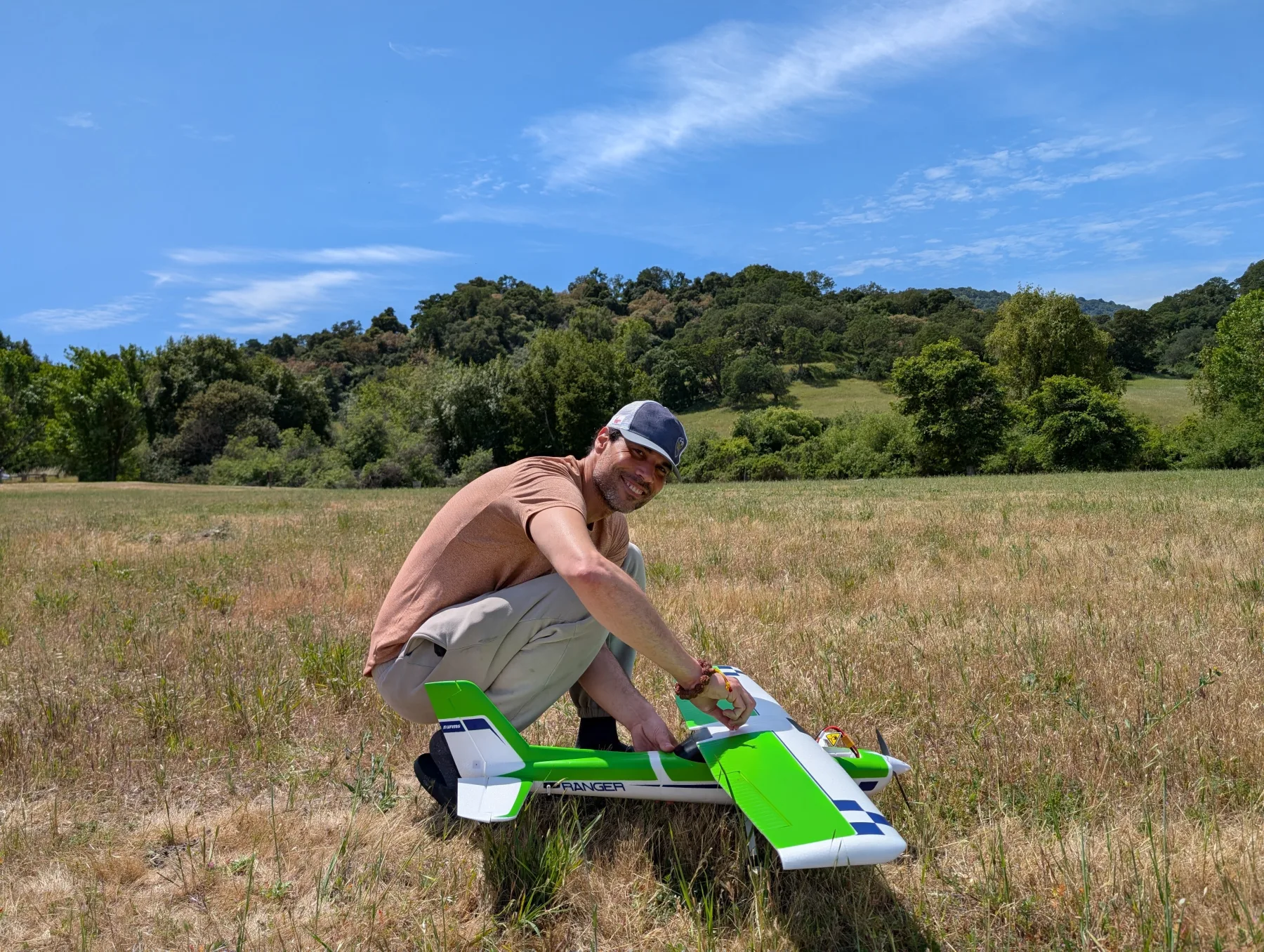 A man kneeling beside a green and white radio-controlled airplane in a field