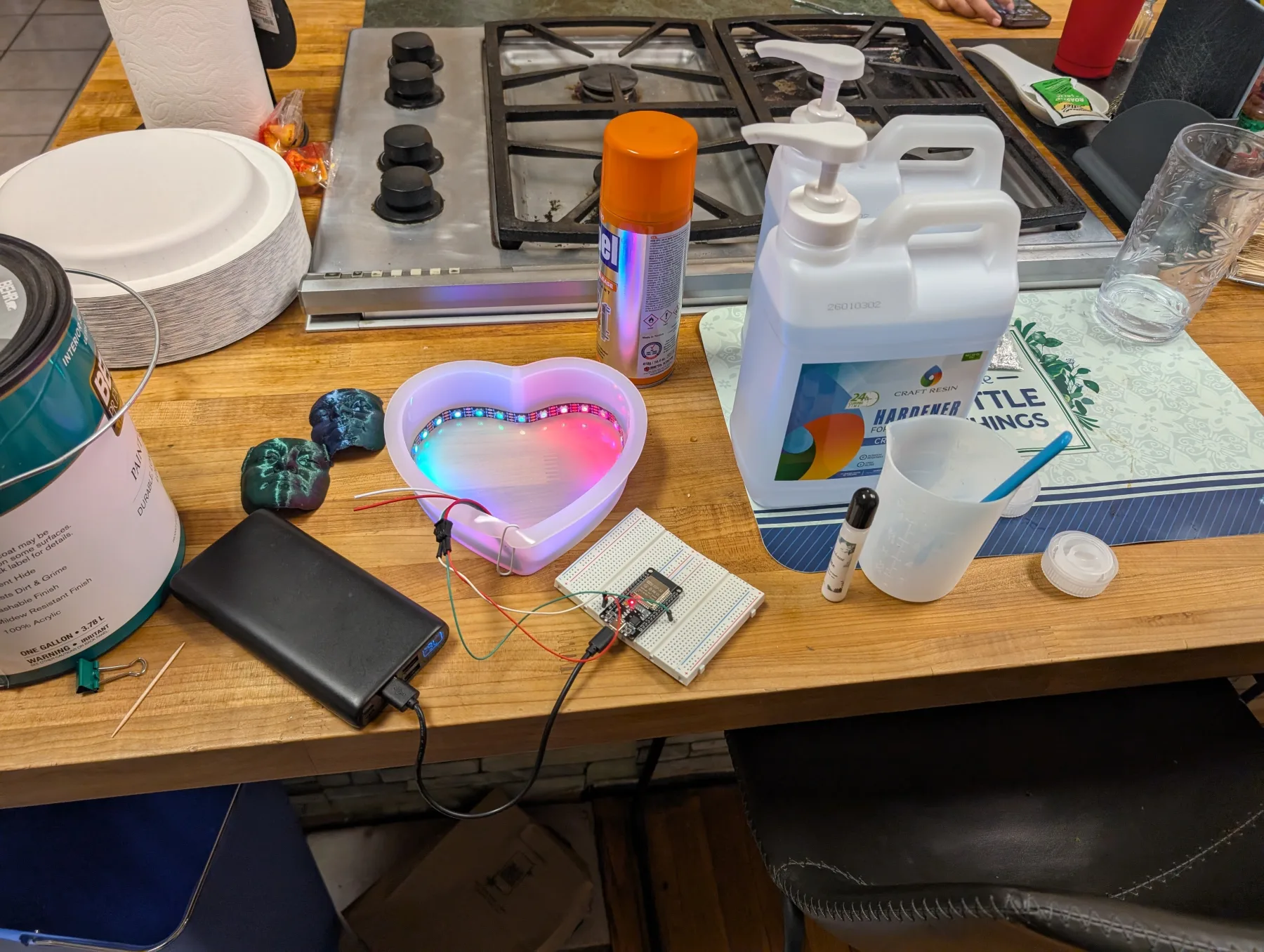 A glowing heart-shaped resin mold, electronics, and resin supplies on a worktable