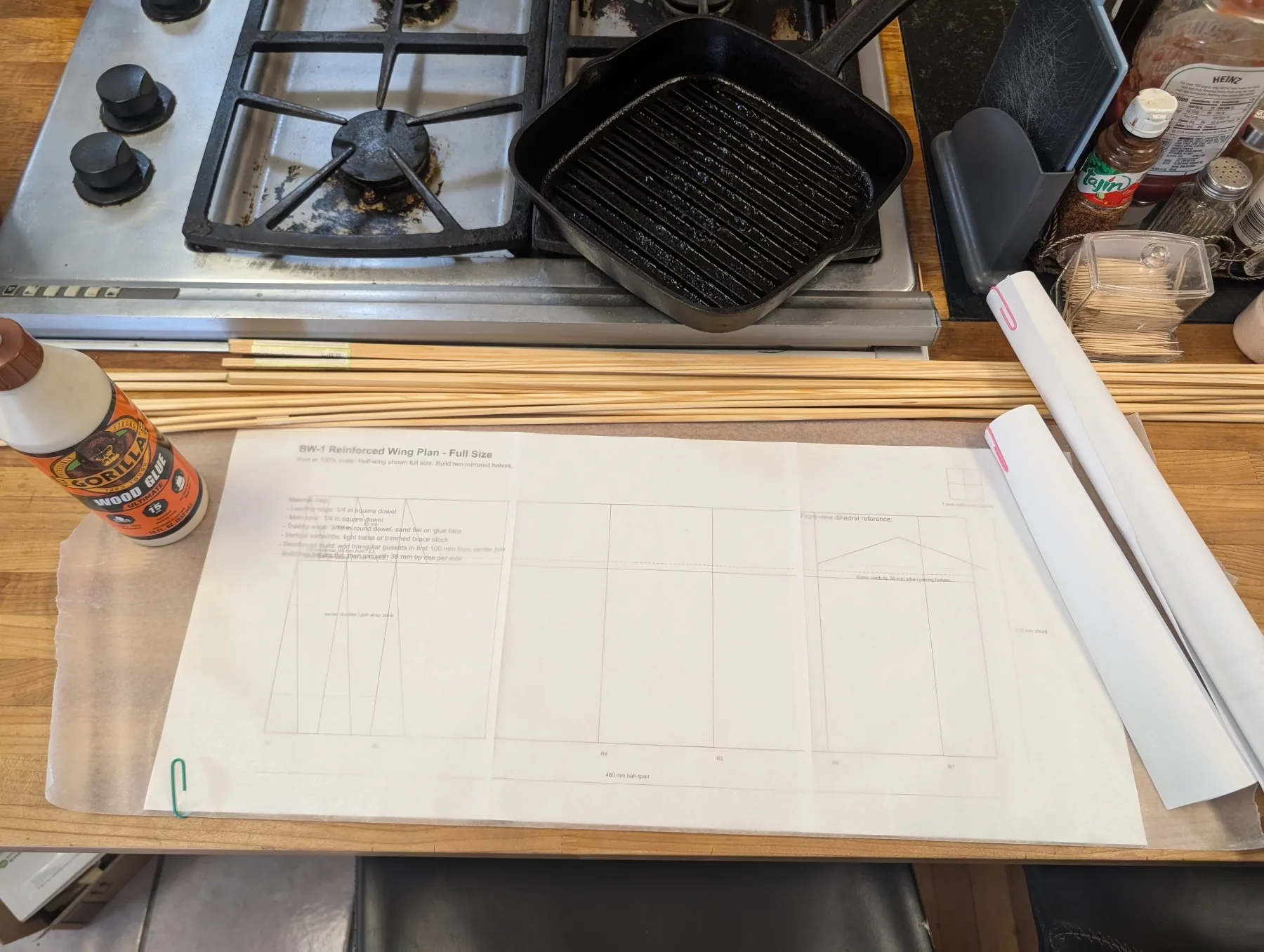 Full-size RC airplane wing plans, wooden spars, and building supplies arranged on a table